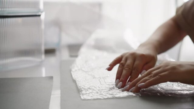 Woman pops bubbles on bubble wrap in hands and puts protective packaging film on table. Young female relieves stress with monotonous movements closeup