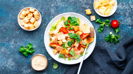 Gourmet Caesar salad with shrimp, tomatoes, iceberg lettuce, croutons, parmesan cheese and caesar dressing. Blue table background, top view