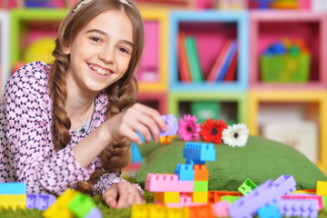 Portrait of cute girl playing with colorful plastic blocks in room