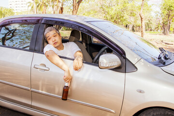 Young asian driver sits in a car holding a beer bottle, drinks alcohol from a drunken party and can't continue driving. Park on the side of the road for safety : Concept of not drinking and driving. - obrazy, fototapety, plakaty