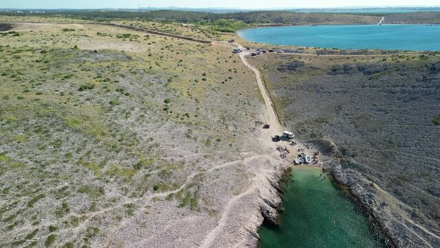 Wide aerial panorama over wild natural cove with beach, a dirt road leading to other side with blue bay sea water in Zadar region, Vrsi.