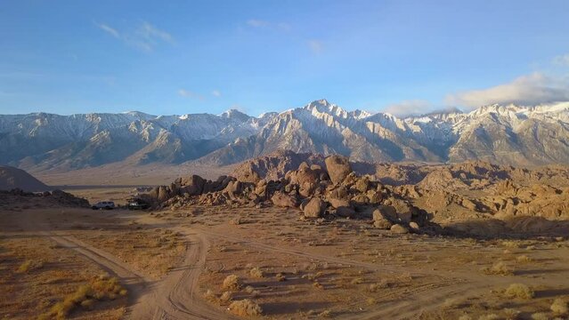 Aerial Backward Shot Of Rocks On Land With Mountains In Background Against Sky, Drone Flying Over Landscape - Alabama Hills, California
