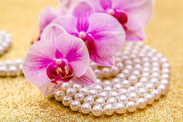 Obraz na płótnie Canvas purple Orchid and pearl necklace on a shiny gold background 