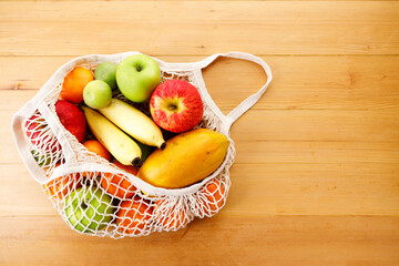 Cotton mesh grocery bag with fresh fruits lying on wooden table.