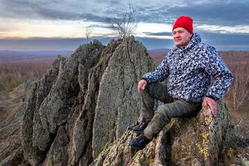 handsome mature man sits on a high rocky mountain and looks into the distance