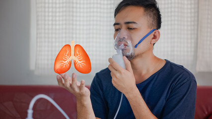 Asian boy wearing oxygen mask.  man using asthma inhaler while sitting at home due to allergy. Asia...