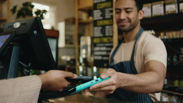 Young multiracial man working as greengrocer at checkout taking payment from customer in greengrocer's shop