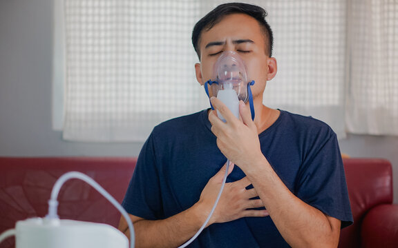 Asian boy wearing oxygen mask.  man using asthma inhaler while sitting at home due to allergy. Asia man using spray asthma.
