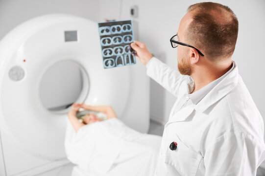 Medical computed tomography or MRI scanner. Close up of doctor holding and examining results of MRI. Woman patient lying on couch. Concept of medicine, healthcare and modern diagnostics.