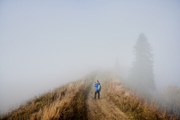 Obraz premium Photographer taking picture with professional camera while standing on grassy hill road with dense fog on background