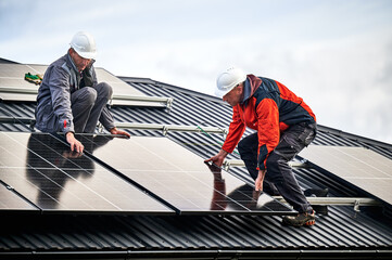 Technicians building photovoltaic solar module station on roof of house. Men electricians in...