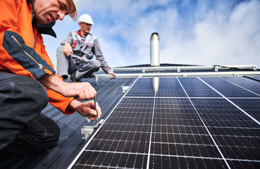 Workers installing photovoltaic solar panels on roof of house. Men engineers in helmets building...