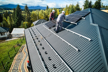 Technicians installing solar panel system on roof of house. Men workers in helmets carrying...