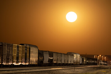 Moon rise as an orange glowing sphere over freight train