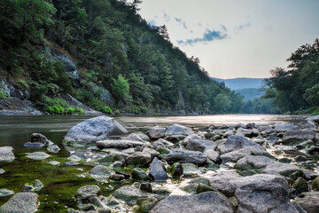Tranquil river lined with rocks and lush trees at sunset.