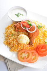 traditional Indian fragrant yellow ginger nasi biryani rice with tandoori chicken drumlet, poached egg and yogurt sauce salad in plate on white background asian halal food cuisine menu for cafe design