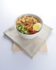 Malay mee rebus noodle with boiled egg, tofu, green chilli, sambal, vegetable, chilli sauce and hot thick spicy gravy soup in bowl on white background asian halal food cuisine menu for cafe design