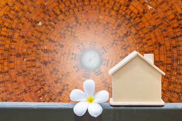 Wooden house model with Plumeria flower over blurred Feng Shui compass plate background, fengshui...