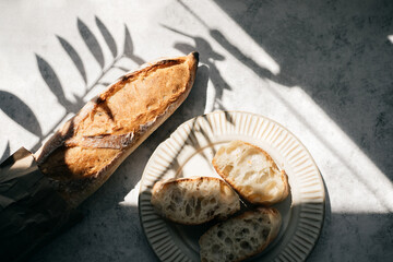 French fresh bread baguette with slices on a ceramic plate on gray background.
