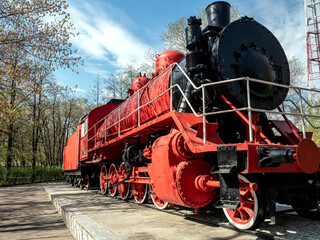 bright red steam locomotive in the city park in the form of a historical monument