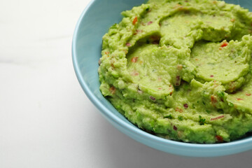 Bowl with delicious fresh guacamole on white table, closeup. Space for text