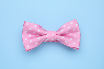 Stylish pink bow tie with polka dot pattern on light blue background, top view