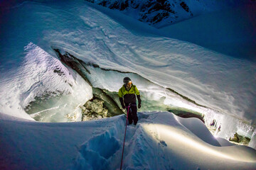 climber on rope rappelling into glacial ice cave