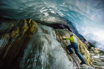 Man climbs frozen waterfall in ice cave below glacier