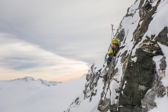 Backcountry skier climbs cliff face towards summit