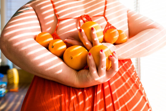 holding seven oranges behind their back in an orange dress