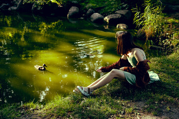 A girl in a mint dress by the lake feeds a duck from her hand