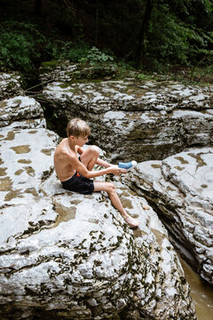 Boy sitting on rock above natural spring in swim attire putting