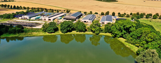 Modern farm with buildings that have solar panels behind a pond in Germany