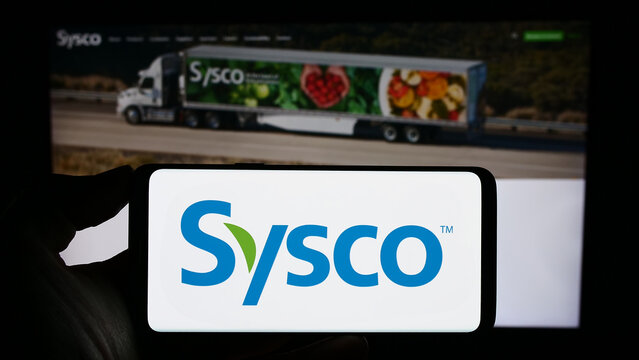 Stuttgart, Germany - 08-09-2023: Person holding smartphone with logo of US wholesale company Sysco Corporation on screen in front of website. Focus on phone display.