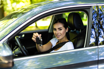 Happy woman sitting inside her new car and showing keys at the dealership
