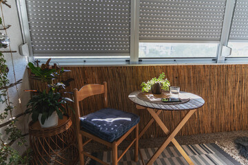 Summer loggia with roller shutters, a chair and a table with a potted plant and a glass of water