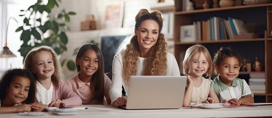 A varied female teacher using a laptop with young schoolgirls in a classroom space for text School learn childhood communicate and educate unchanged