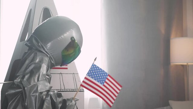 Teen boy in an USA astronaut costume coming out of a cardboard space shuttle, a boy plays an astronaut in the living room of the house.