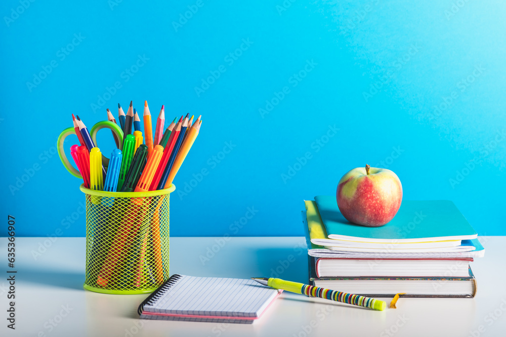 Wall mural A stack of books, a stand with pencils and pens and an open notebook on a blue background. Back to school, teacher's day.