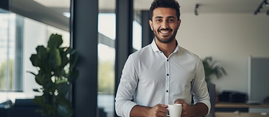 Middle Eastern man smiling and holding coffee cup in office looking at camera