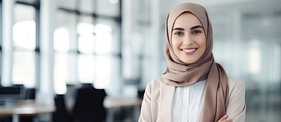 Fototapeta na wymiar Confident young Muslim woman in modern office wearing a headscarf smiling at the camera waist up