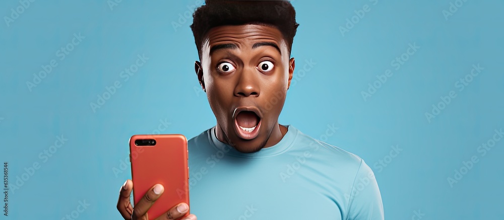 Wall mural Surprised African man with short hair holds smartphone with mockup on background