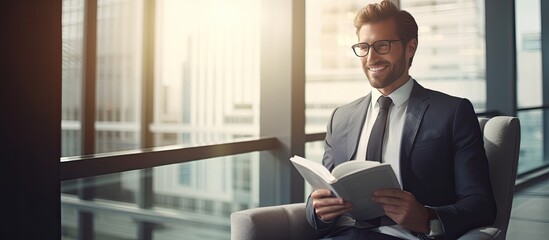 Fototapeta premium Positive young businessman in modern corporate setting looking at camera with diary sunlight through windows