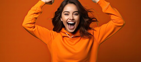 Enthusiastic young woman playfully imitates a rider dances energetically and happily points upwards dressed casually posing in a studio with an orange bac