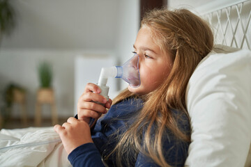 Elementary age girl  using nebulizer in bed at home