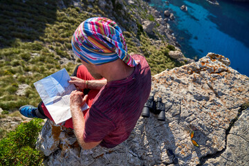 Unrecognizable hiker reading map on cliff - Powered by Adobe