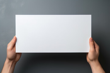 A human hand holding a blank sheet of white paper or card isolated on grey background
