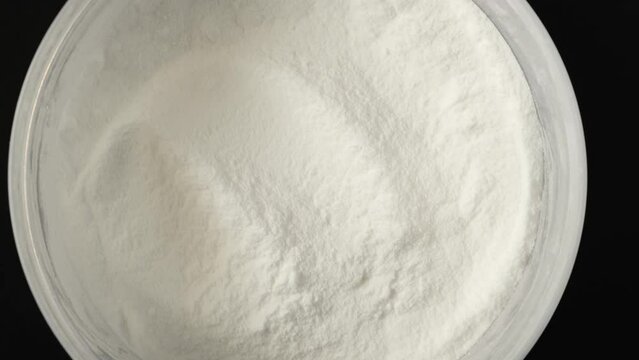 Succinic acid or dicarboxylic acid in plastic container, close-up, top view. Spirit of amber, white powder, chemical formula C4H6O4, Food additive E363. Video 4K, Rotating.