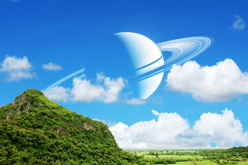 Saturn near earth back on the blue sky and white cloud over mountain and green field