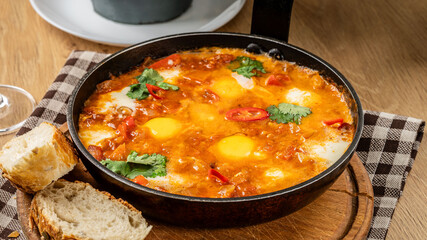 Traditional oriental cuisine. Arabic dish Shakshuka. Turkish breakfast, fried eggs, tomato sauce, peppers, cilantro and 2 pieces of baguette.